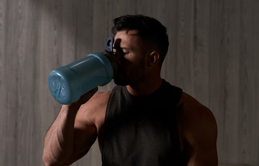 Man in dark lit gym drinking from blue Koda 74oz bottle